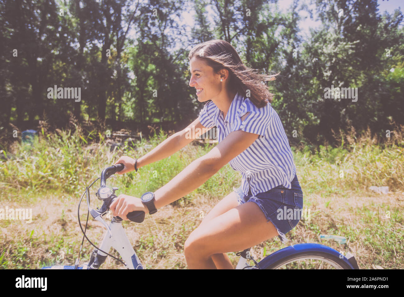 Smiling pretty young woman in jeans shorts riding bicycle in the park