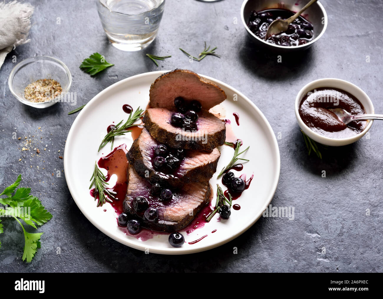 Tasty beef with blueberry sauce on white plate over blue stone background. Medium rare roast beef with berry sauce. Stock Photo