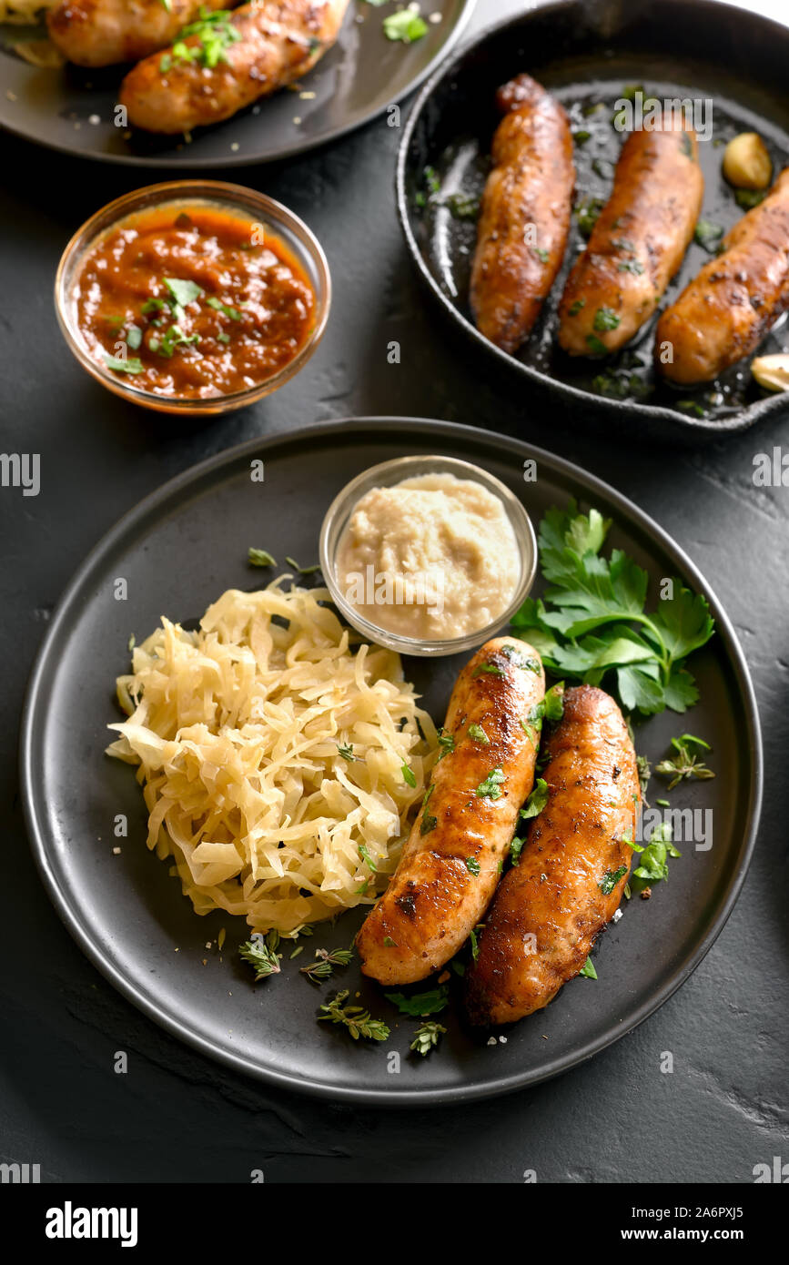 Grilled sausages with sauerkraut and horseradish on plate over black ...