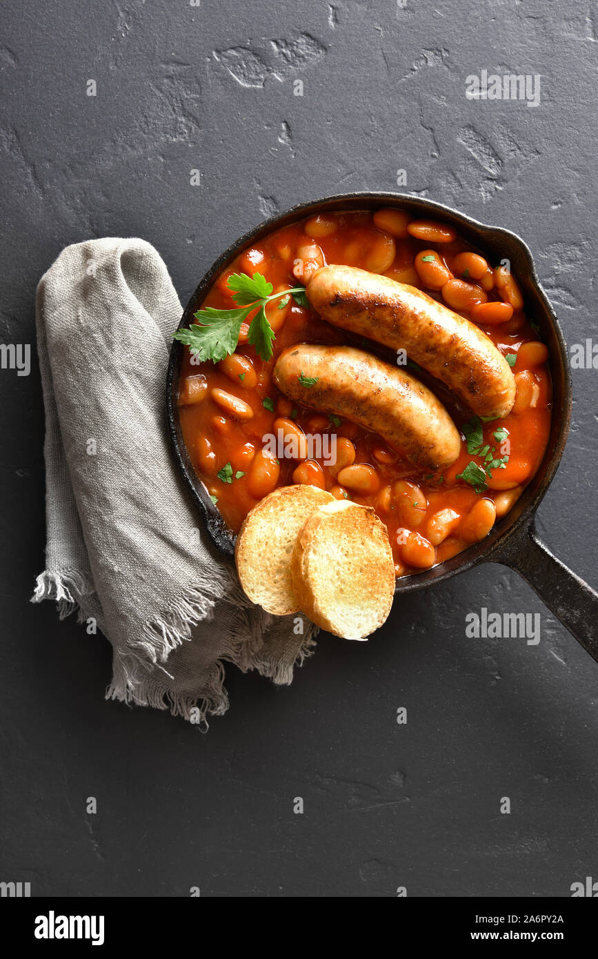 Grilled sausages with baked white beans in tomato sauce in frying pan