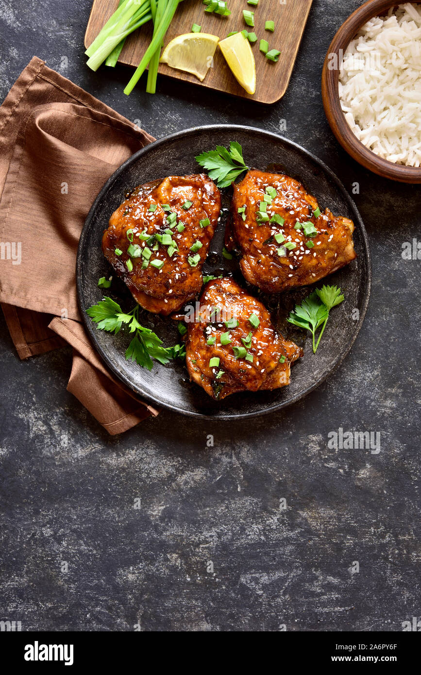 Sweet and spicy honey grilled chicken thighs and bowl of rice over dark stone background with free space. Tasty food in asian style. Top view, flat la Stock Photo