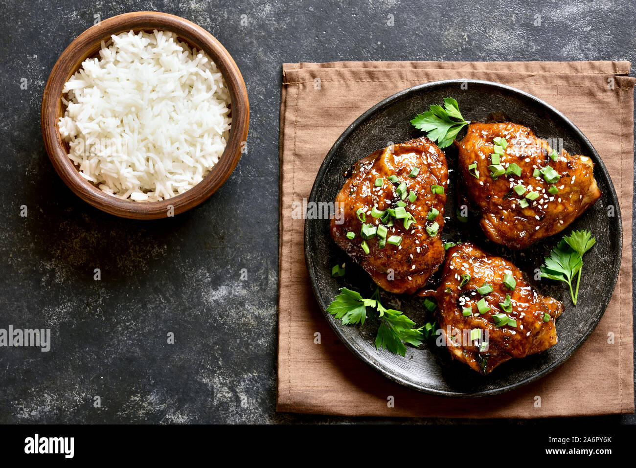 Grilled chicken thighs and bowl of rice over dark stone background