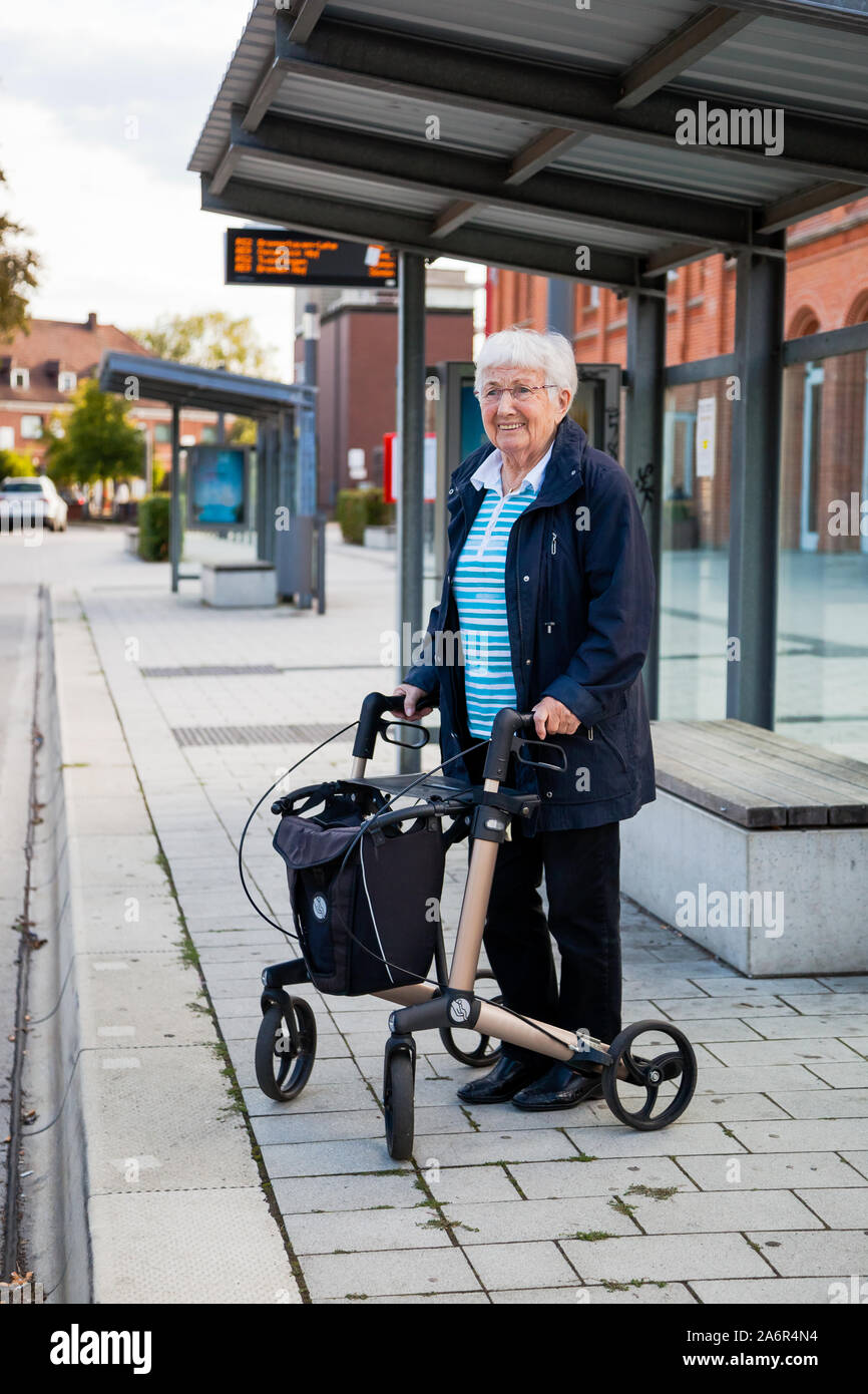 Over 90 years old active senior lady waiting for the bus at the bus stop alone, with walking frame Stock Photo