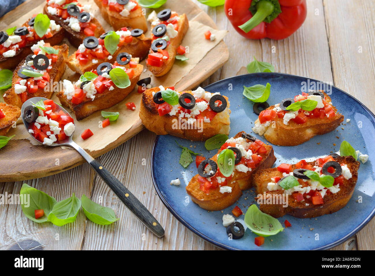Warm Greek bruschetta: Crispy baked small slices of pita bread with feta cheese, black olives, red peppers and basil, served as an appetizer Stock Photo