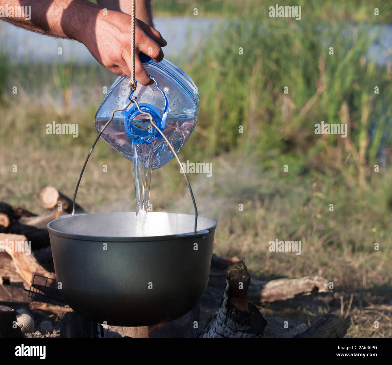 https://c8.alamy.com/comp/2A6R6PG/adding-water-from-big-plastic-bottle-in-black-used-cauldron-on-open-fire-camping-meal-2A6R6PG.jpg