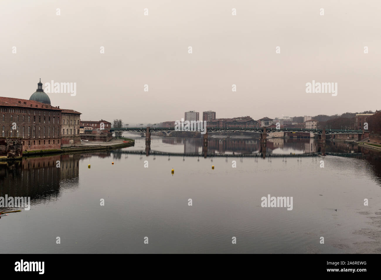 a view of the Garonne River as it passes through Toulouse, France, in a foggy day with the bridge Pont Saint Pierre in the background and the Hotel-Di Stock Photo