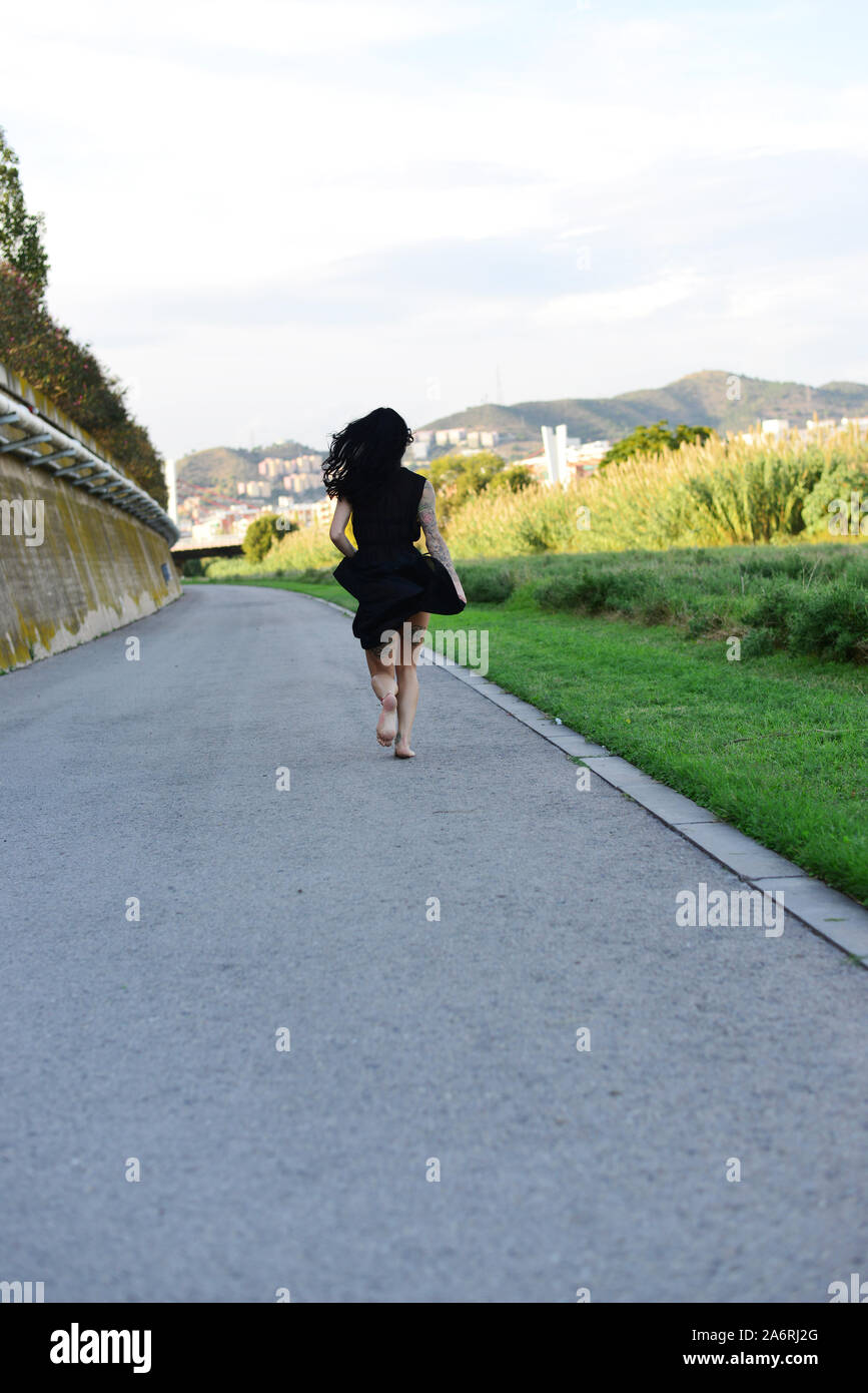 Beautiful young woman in black dress running away Stock Photo