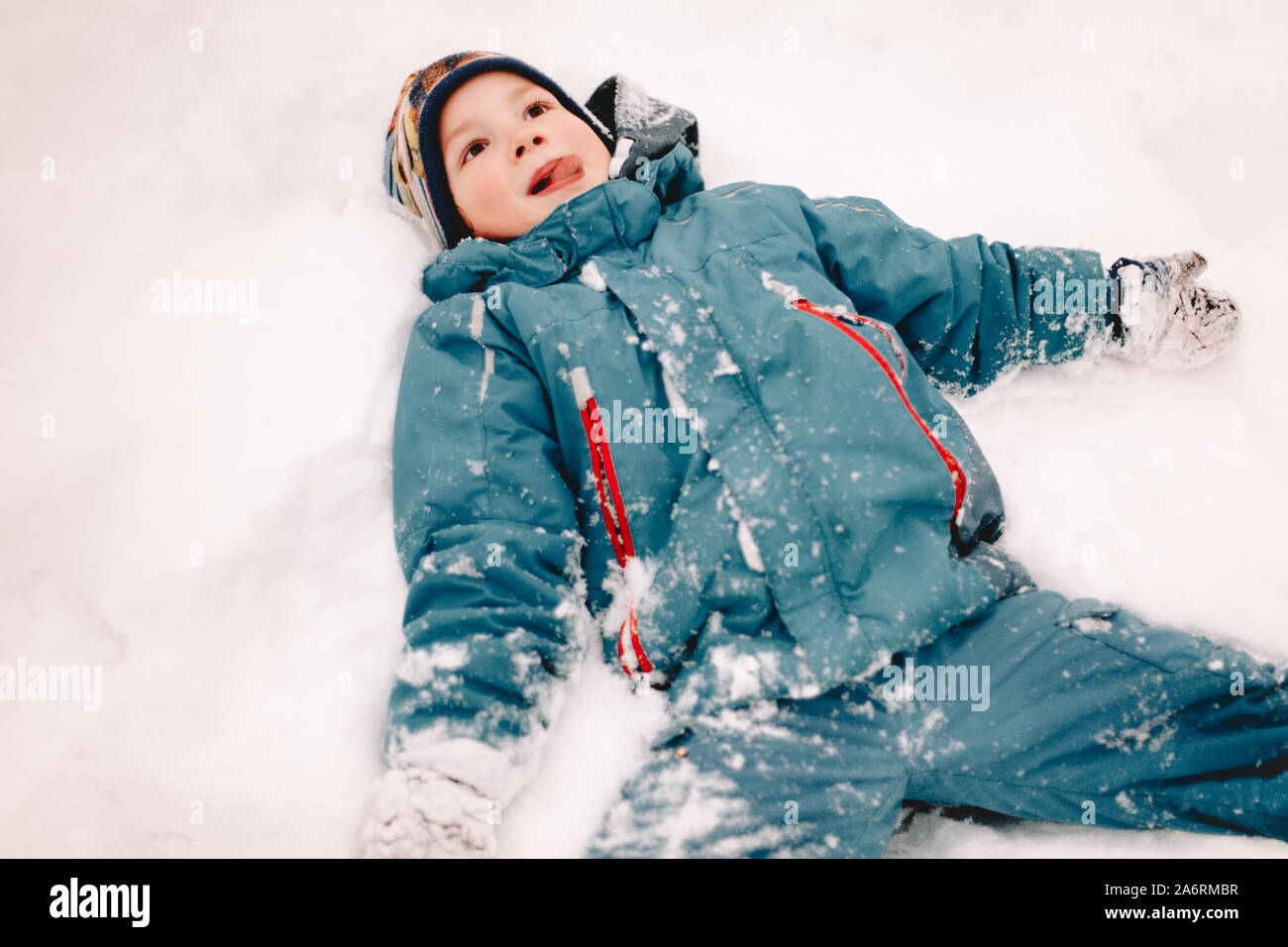 Happy boy with arms outstretched lying in snow during winter Stock Photo -  Alamy