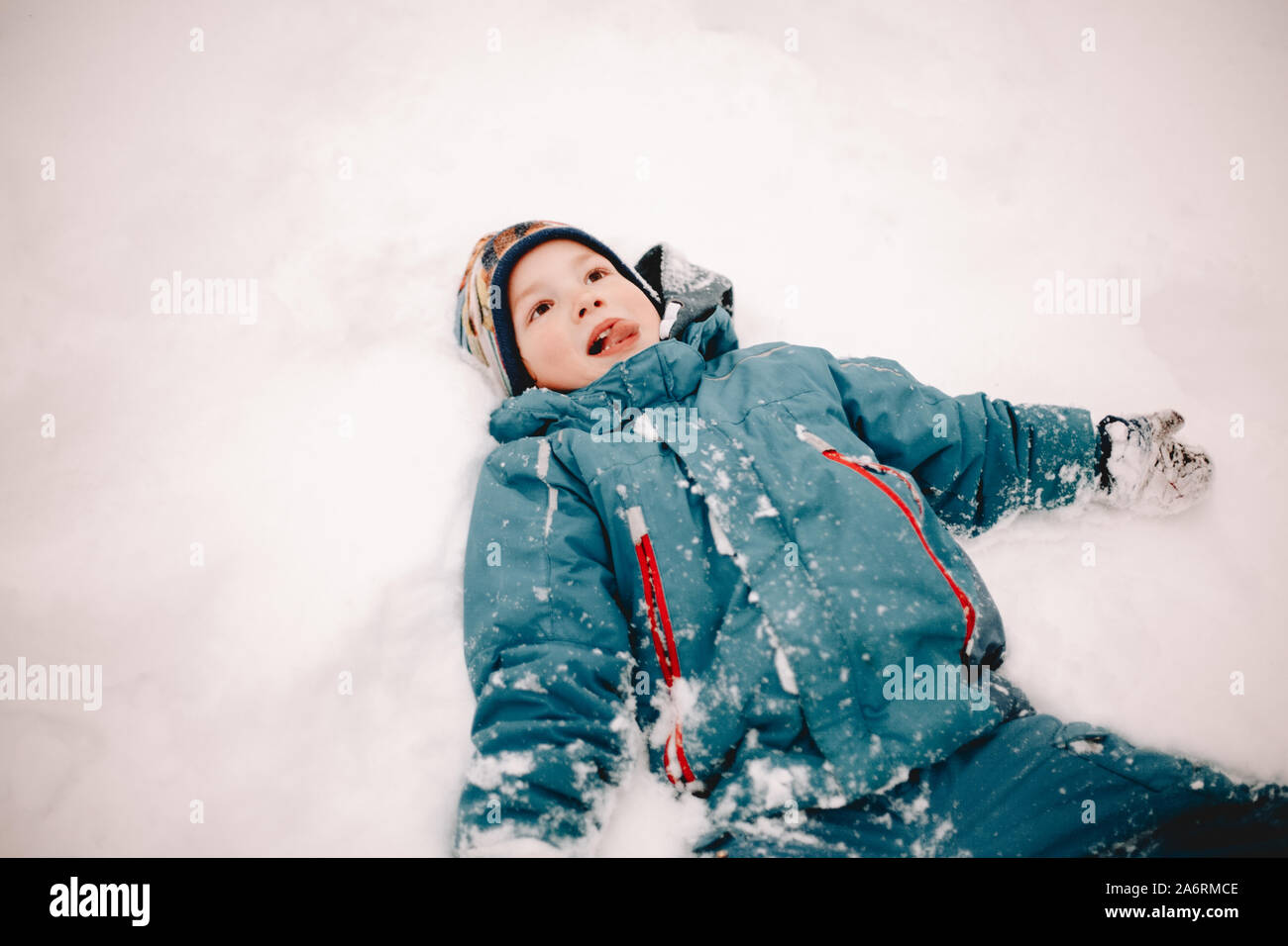 Happy boy sticking out tongue while lying in snow in winter Stock Photo