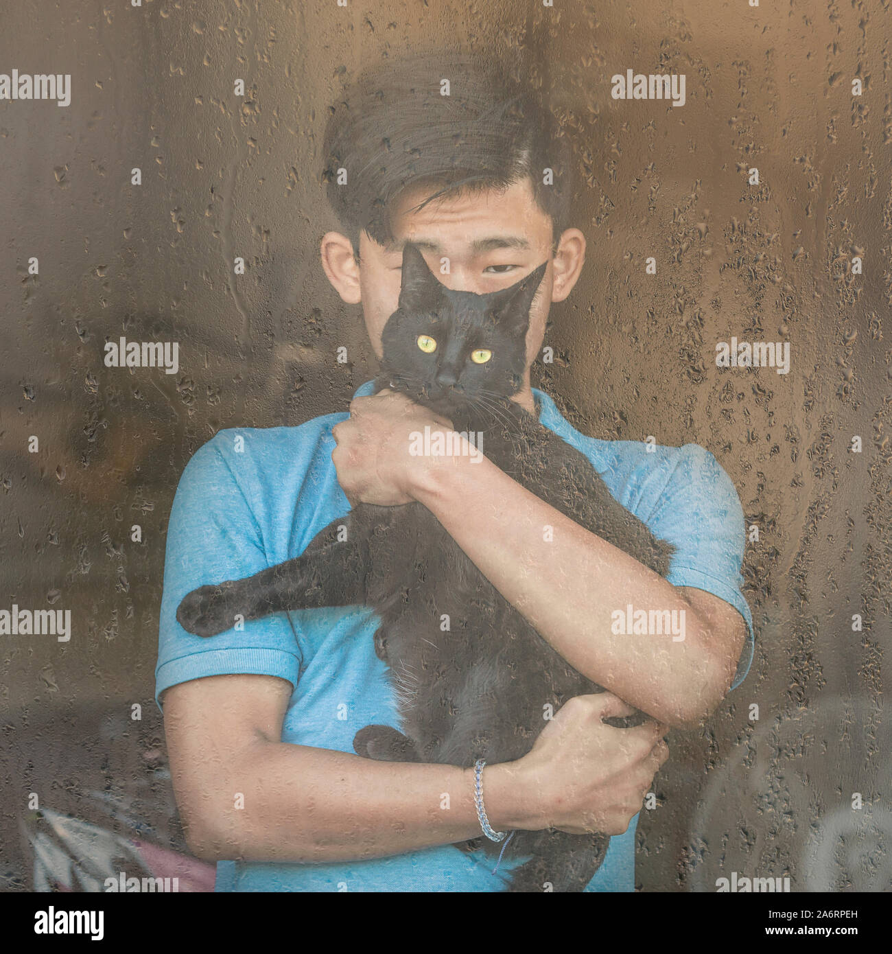 Asian Chinese boy and black cat look out rain streaked window Stock Photo