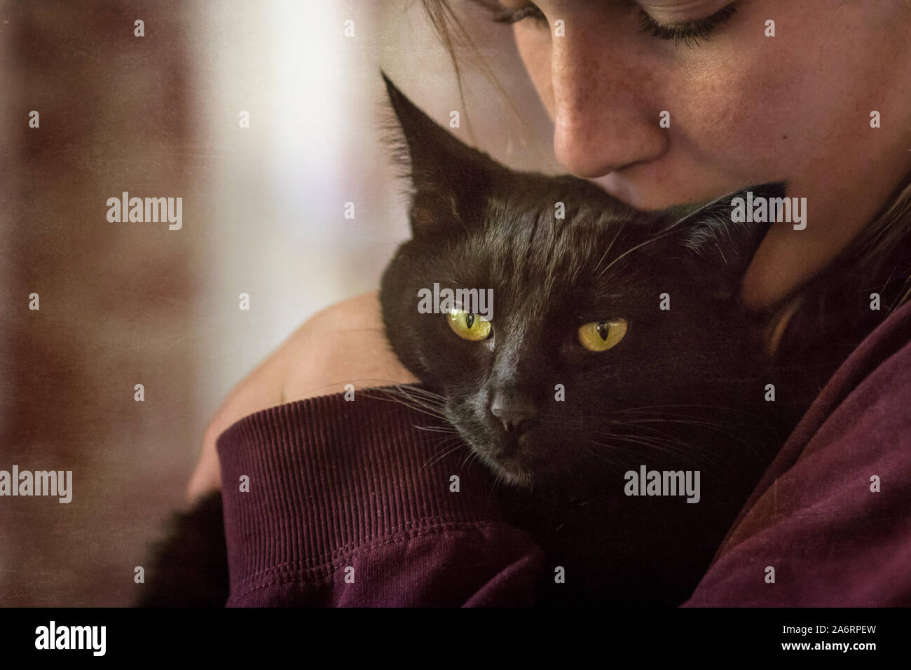 Young girl with freckles snuggles and kisses black cat Stock Photo