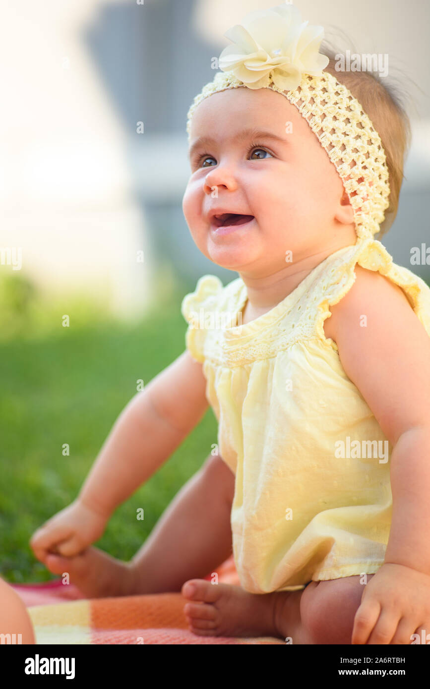 Cute baby girl in yellow band and dress sits in sunny backyard. 8 months  old infant outdoors laughing Stock Photo - Alamy