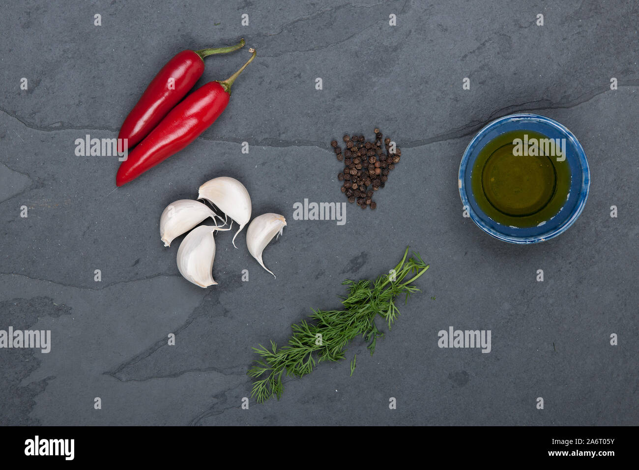 Dill, red peppers, black pepper corn, oil and garlic on a grey slate plate, stock picture Stock Photo
