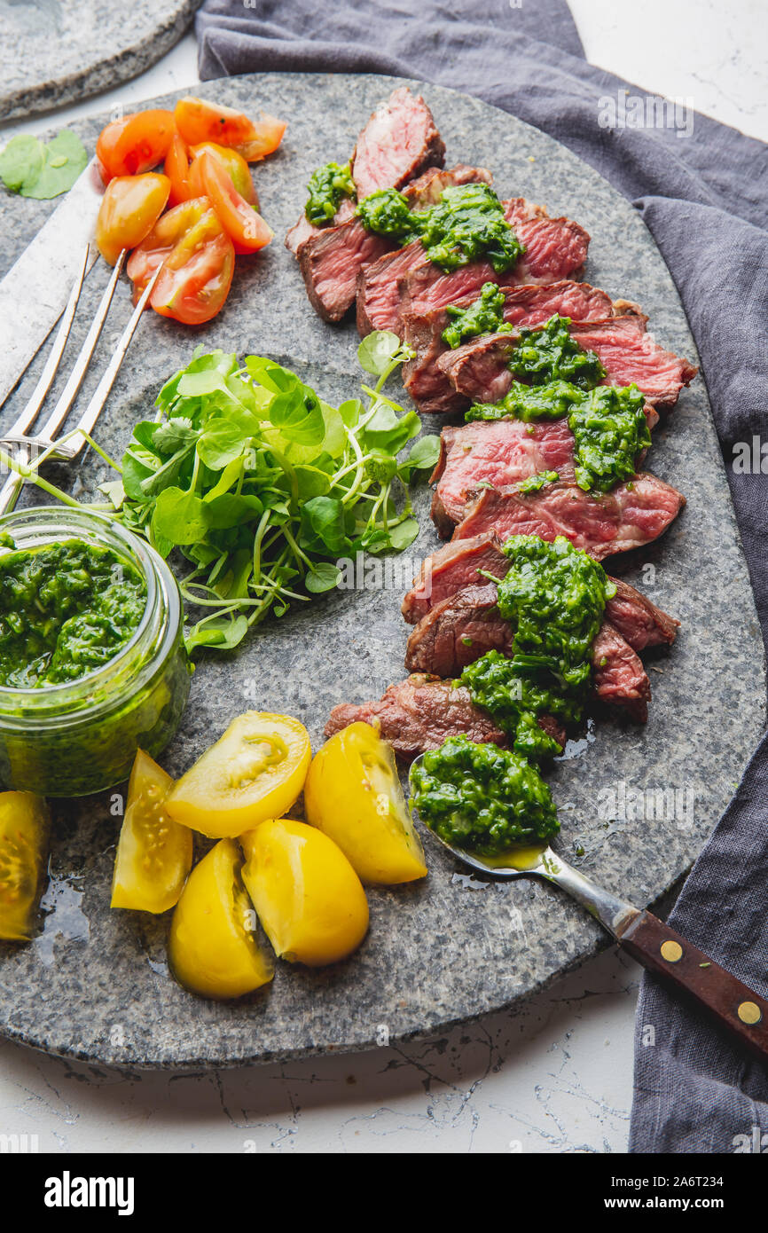 Slices of beef steak with chimmichuri sauce on gray stone plate Stock ...