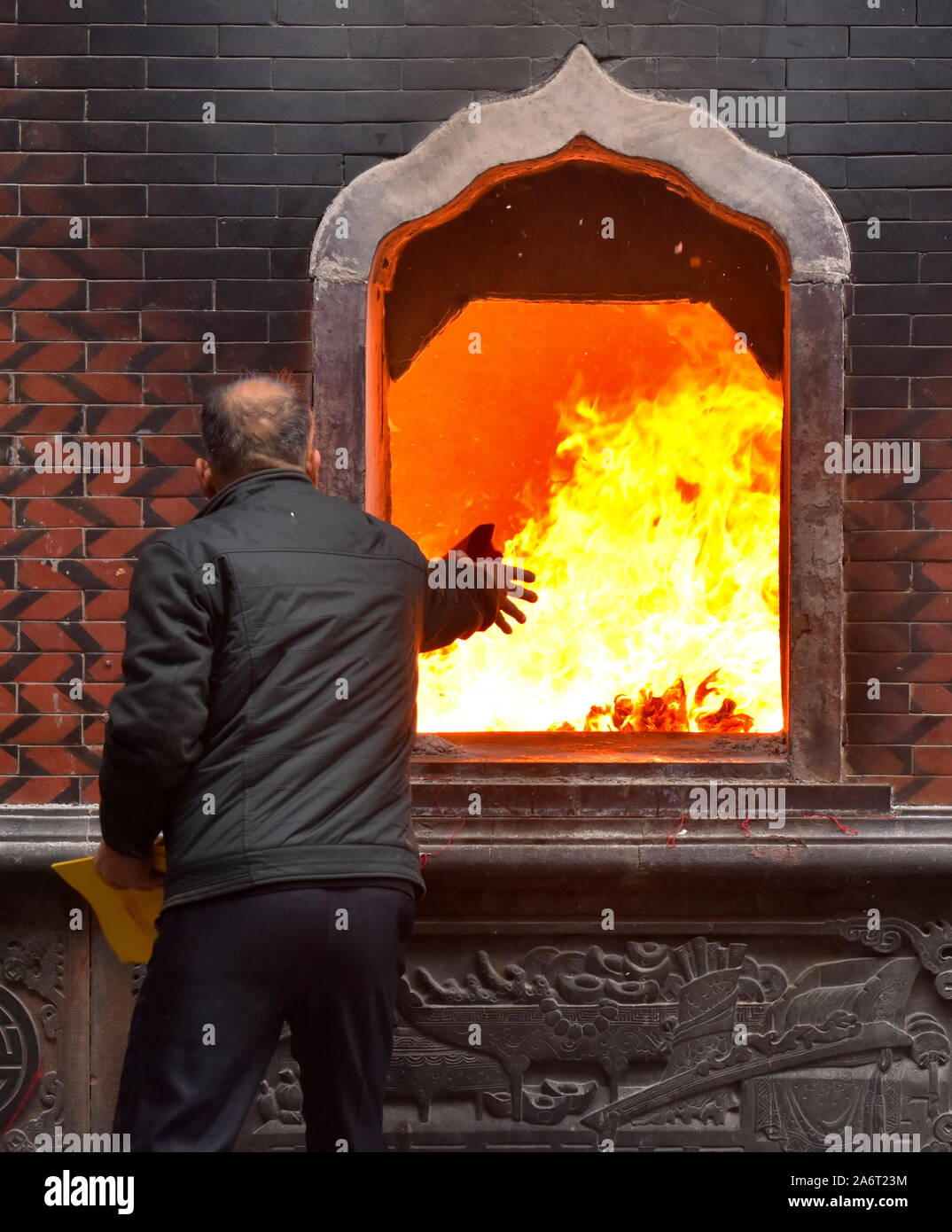 Senior man throws joss paper offerings to burn in fire of Tonghuai Guanyue temple of Chinese native religion in Quanzhou Stock Photo