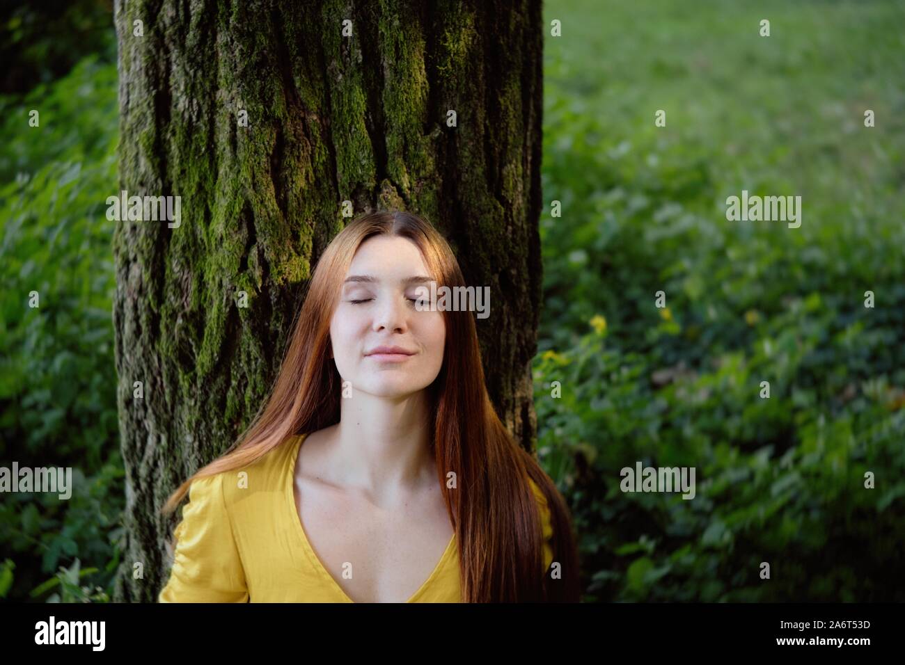 Redhead Woman Leaning On Tree Smiling With Closed Eyes Stock Photo