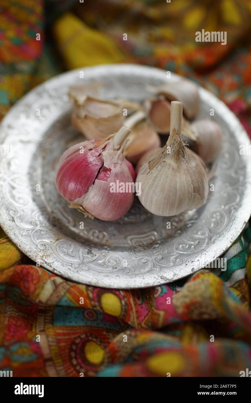 Garlic bulbs with cloves on a silver plate and vintage cloth. Stock Photo