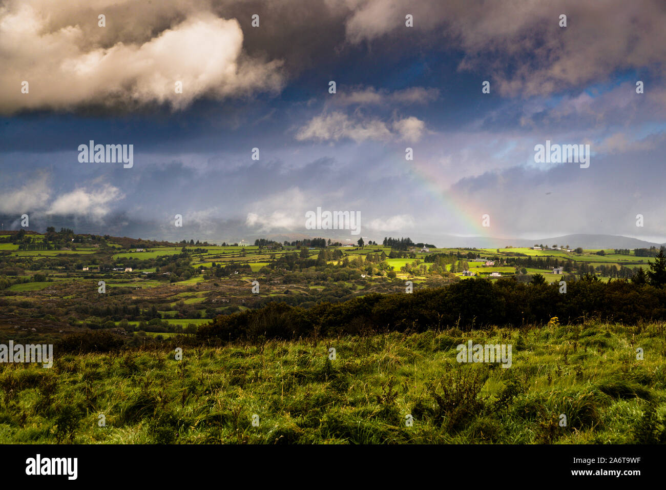 A rainbow stretches over rolling hills and pastureland near Macroom, County Cork, Ireland, as the drive continues from Kilnamartyra towards Killarney and the Gap of Dunloe. Stock Photo