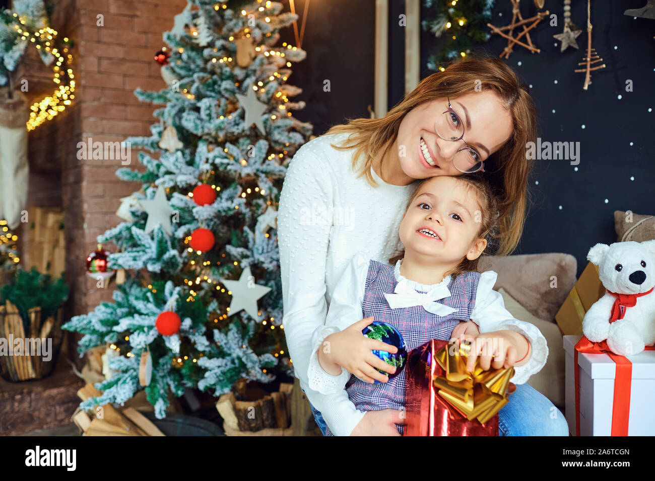 Mother and daughter hugging by the Christmas tree. Stock Photo
