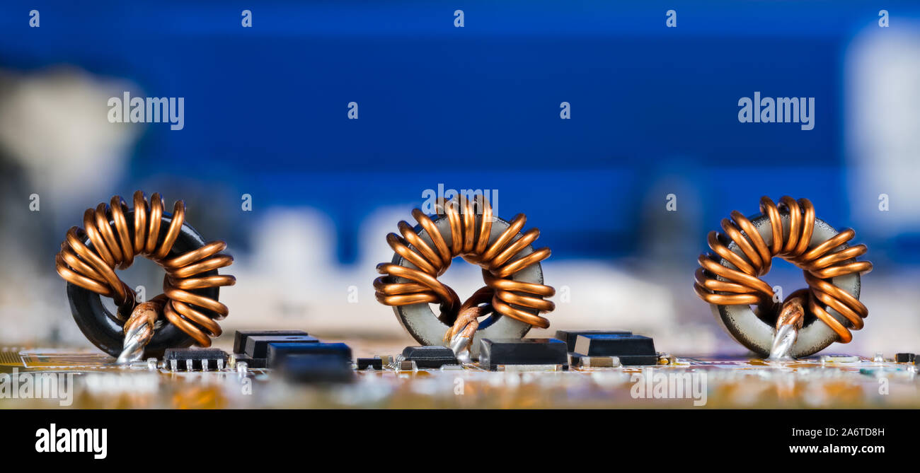 Toroidal inductors with beautiful copper wire winding. Electronic components as coils or transistors on circuit  board detail. Electrotechnical device. Stock Photo