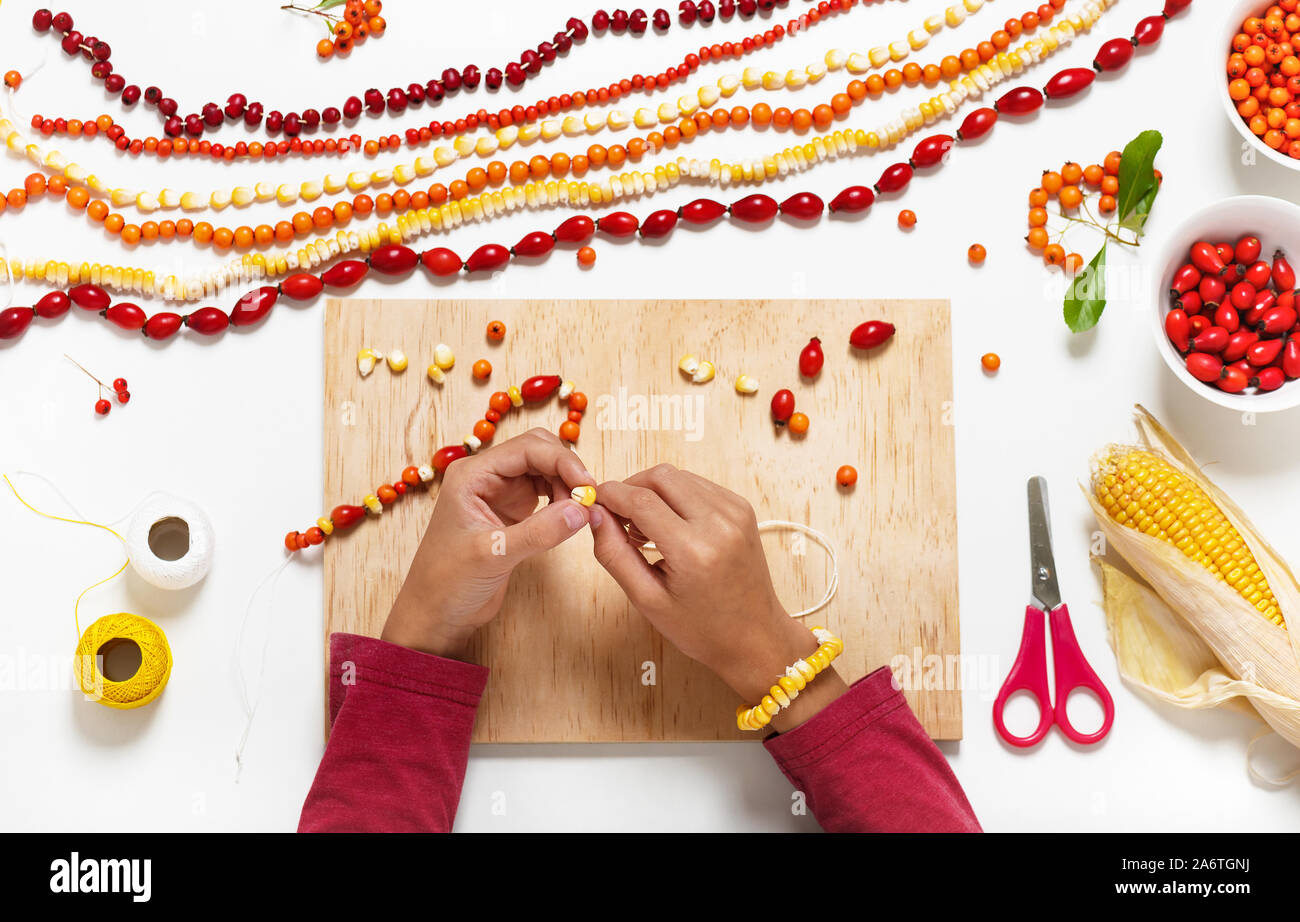 Little child hands make necklace with colorful seeds and forest berries. Stock Photo