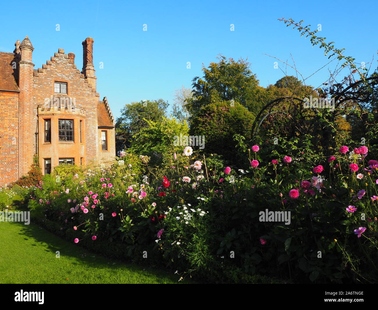 Chenies Manor house, bordered by the plant border stocked with Dahlias, Cosmos and herbaceous plants, west facing windows, on a fine afternoon. Stock Photo
