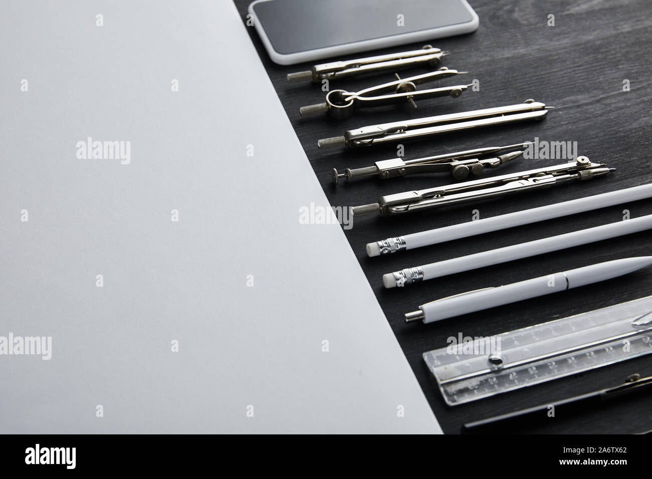 white paper with copy space and compasses, ruler, pencils, smartphone, pen on black and wooden table Stock Photo