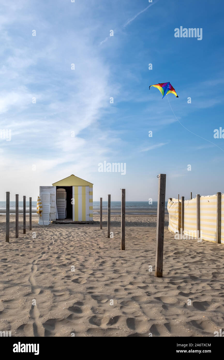 Vintage yellow and white beach hut with multi-colored kite in the sky Stock Photo