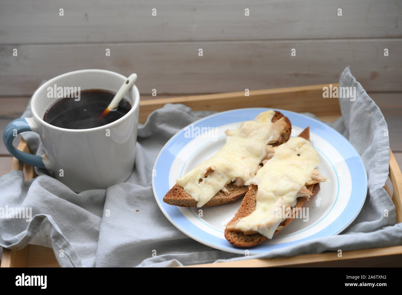 Rustic breakfast: two hot baguette sandwiches with chicken meat and cheese and a cup of black coffee on a wooden tray Stock Photo
