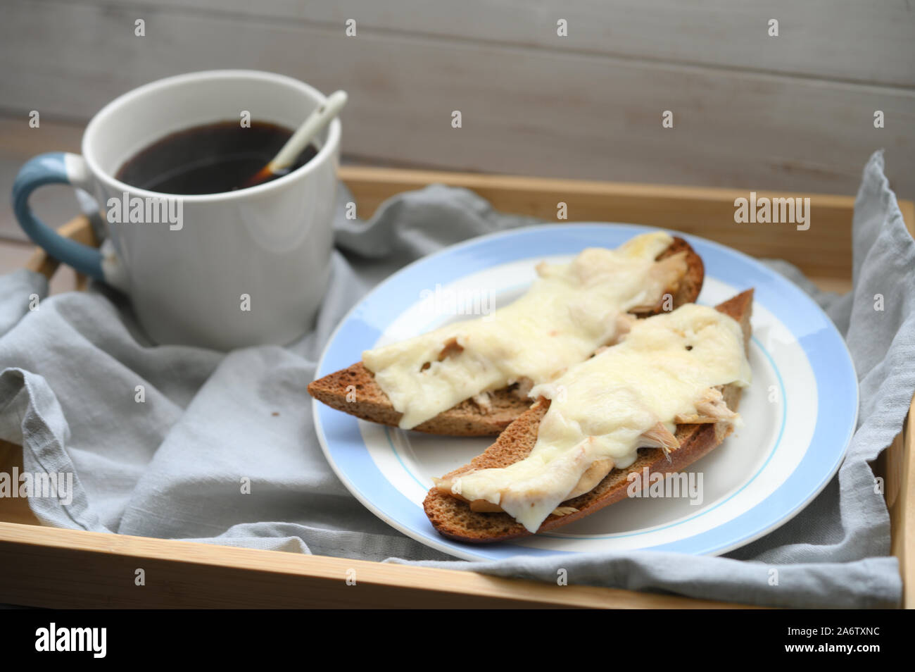 Rustic breakfast: two hot baguette sandwiches with chicken meat and cheese and a cup of black coffee on a wooden tray Stock Photo