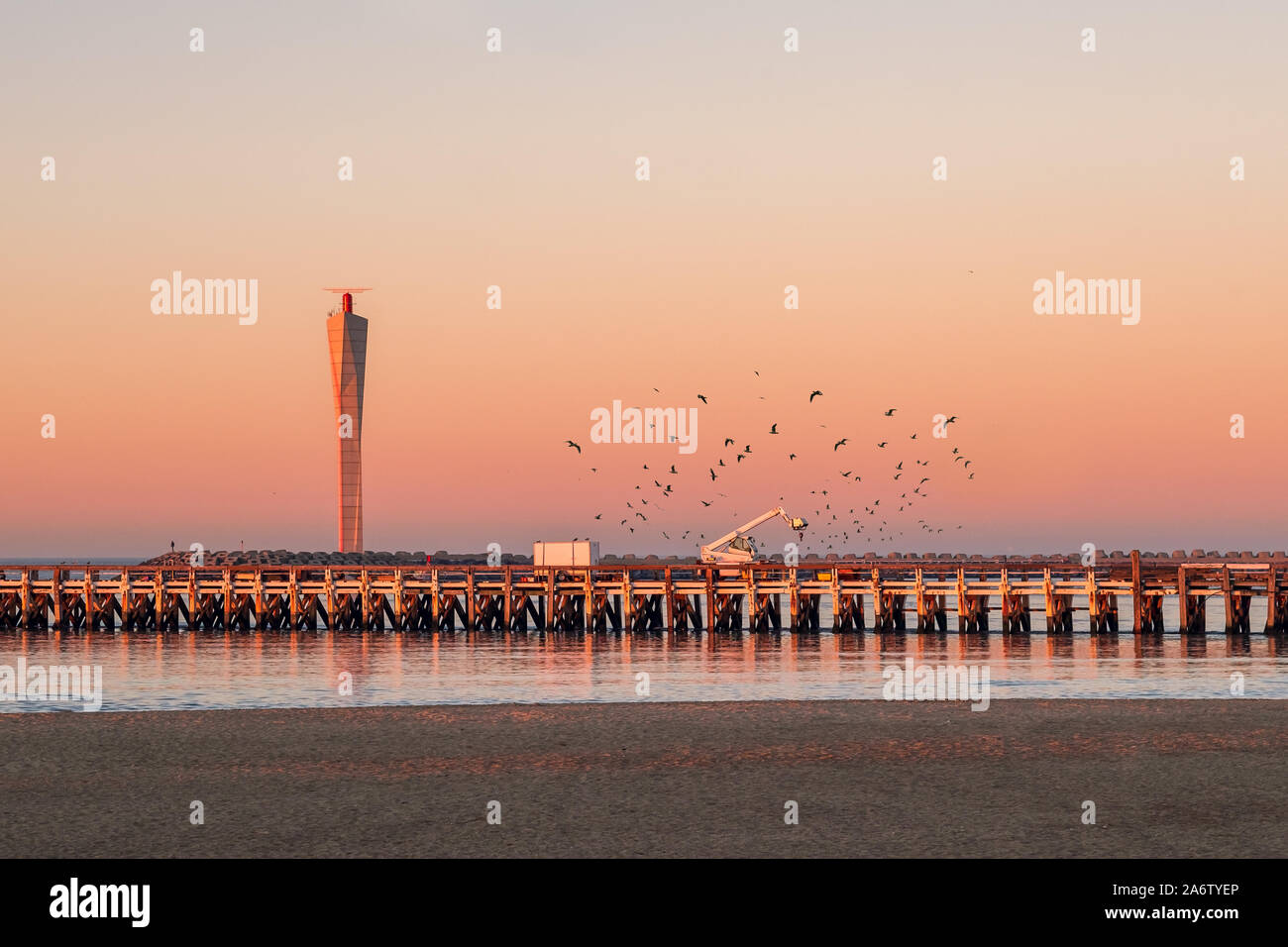 Sunset  on the old wooden pier of Ostend, with modern radar tower in the background. Lots of seagulls flying around. Stock Photo