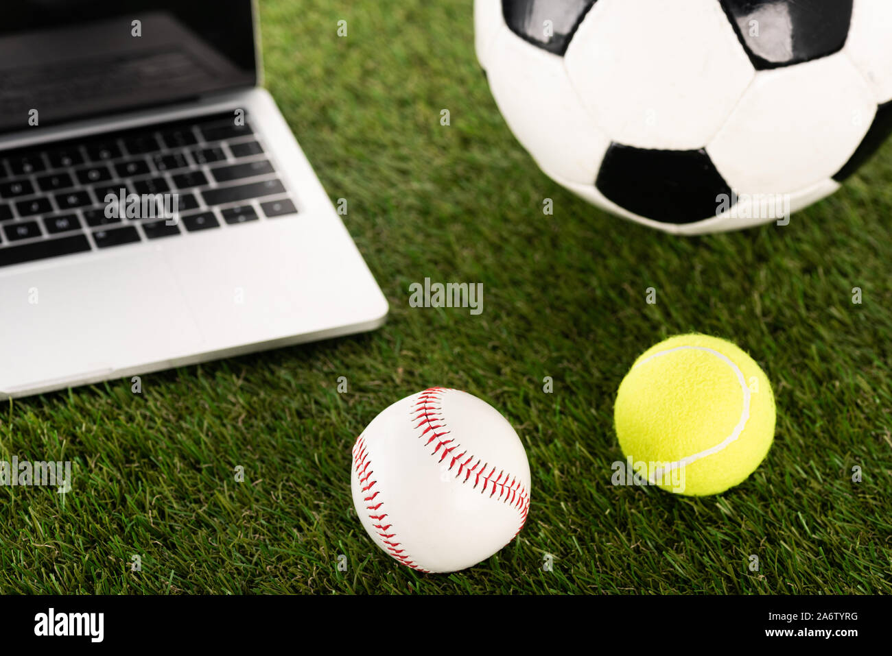 soccer, baseball and tennis balls near laptop on green grass, sports betting concept Stock Photo