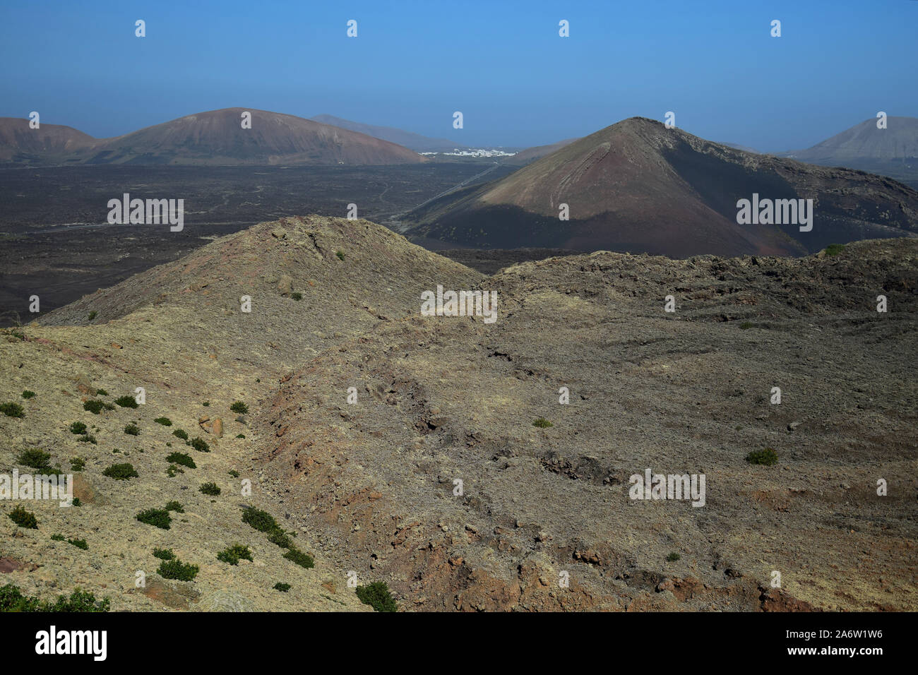 A barren volcano landscape in Lanzarote, Spain. In the distance are the white houses of Mancha Blanca. Stock Photo