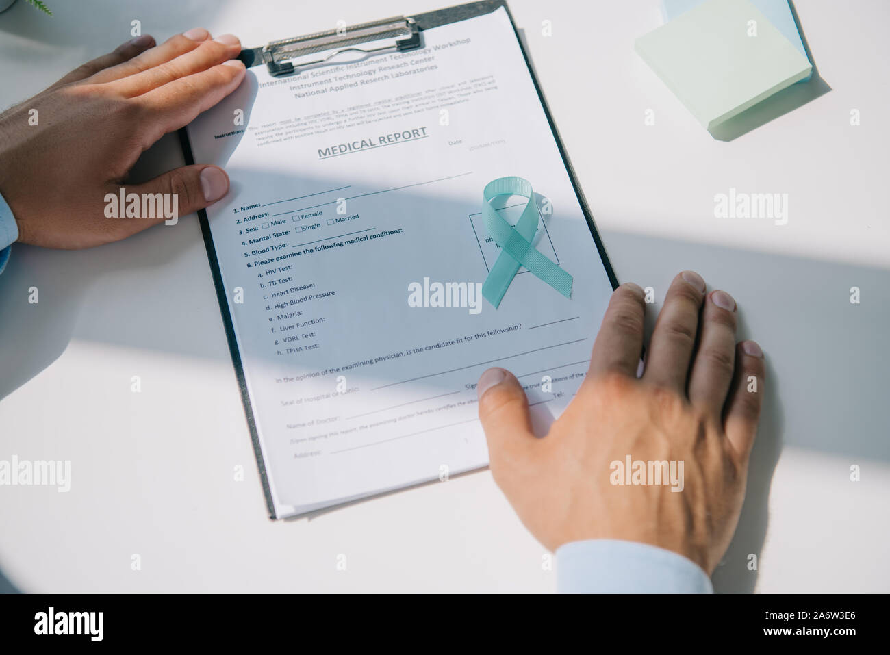 cropped view of doctor sitting at table with blue awareness ribbon on  medical report Stock Photo - Alamy