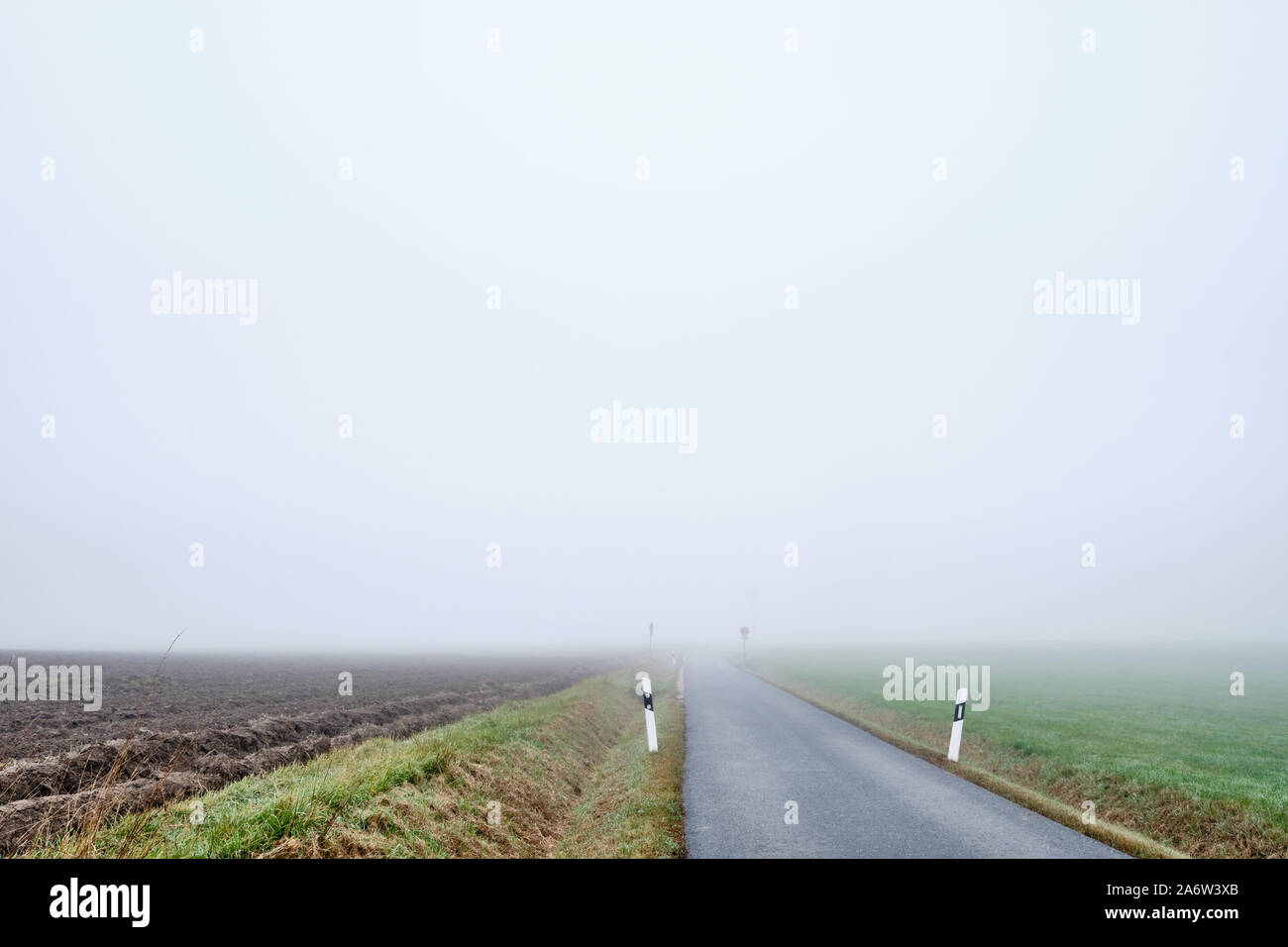 Countryside road to nowhere -  narow street with diminishing perspektive leading into the fog. Seen in Germany near Oedenberg, Bavaria in October. Stock Photo