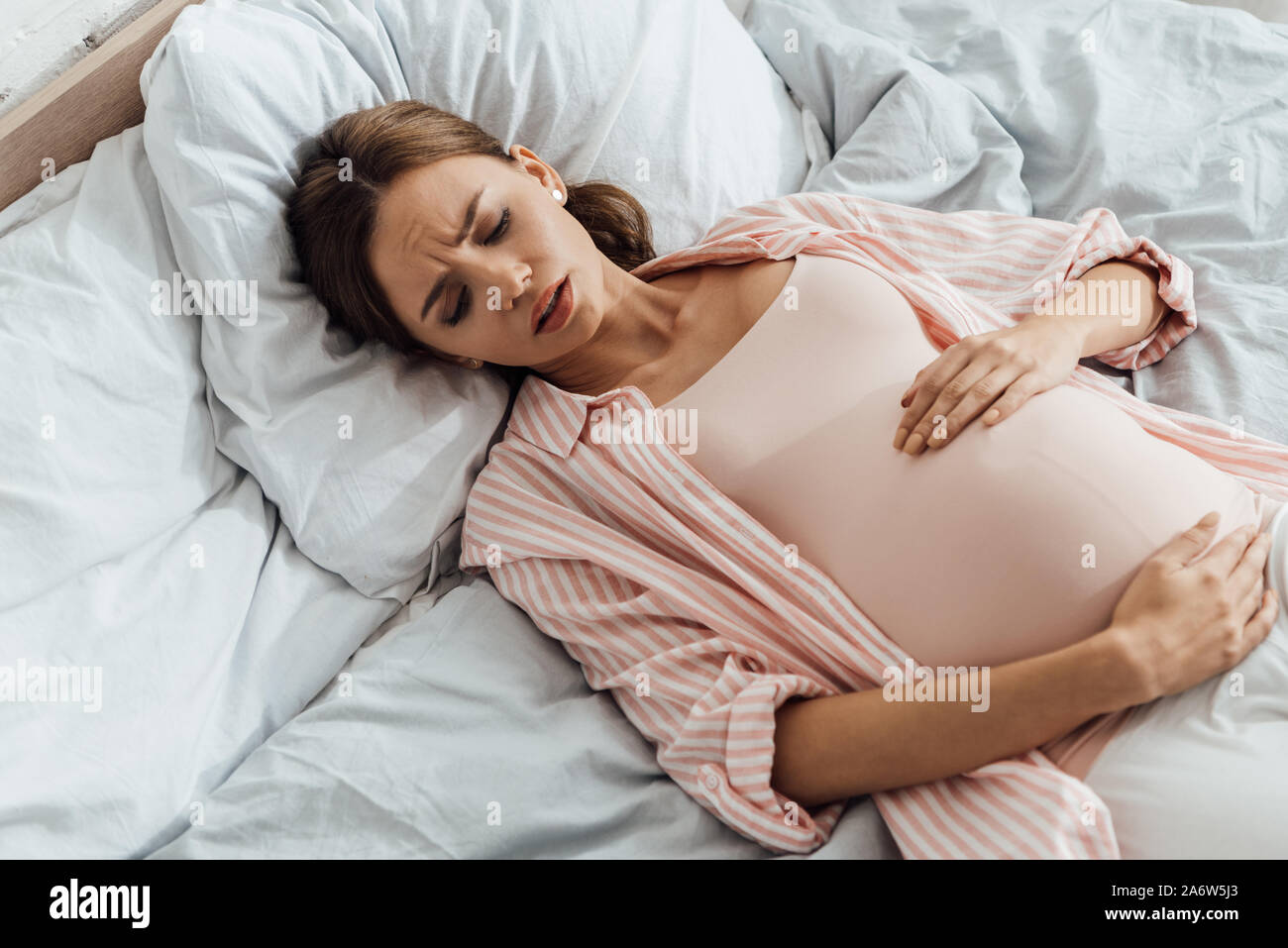 overhead view of emotional pregnant woman lying in bed with grimace and