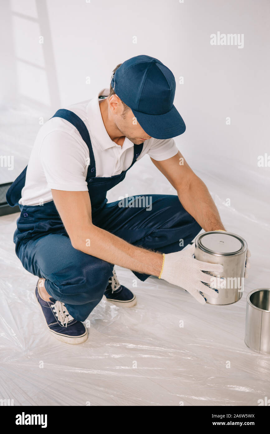 young painter in overalls and cap holding can with paint Stock Photo