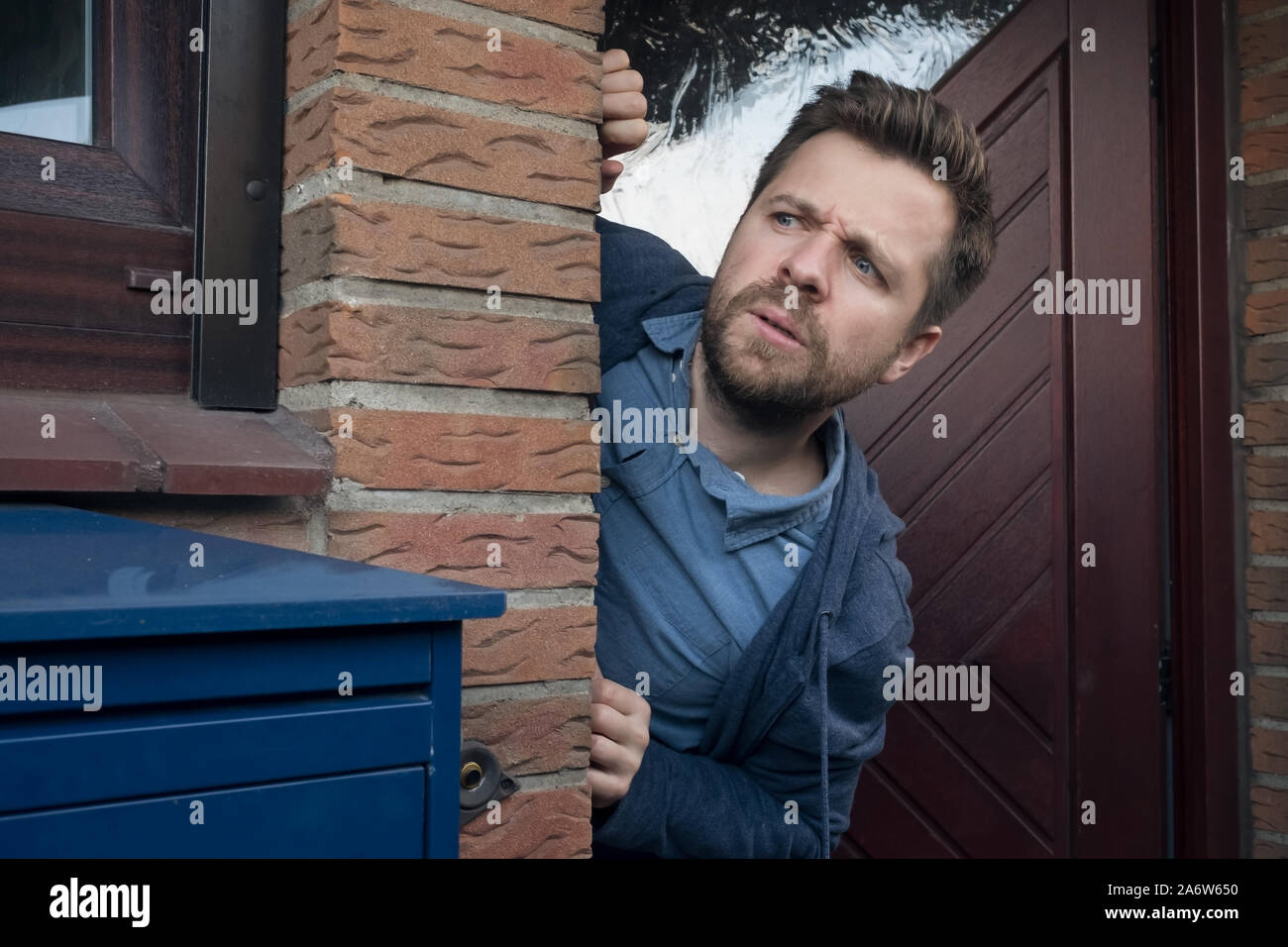 Handsome young man opening door looking on what his neighbor is doing suspecting something. Stock Photo