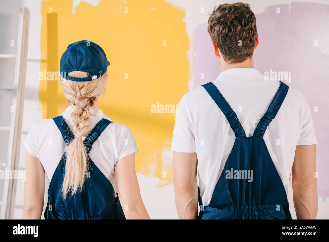 back view of young painters in overalls looking at wall painted in