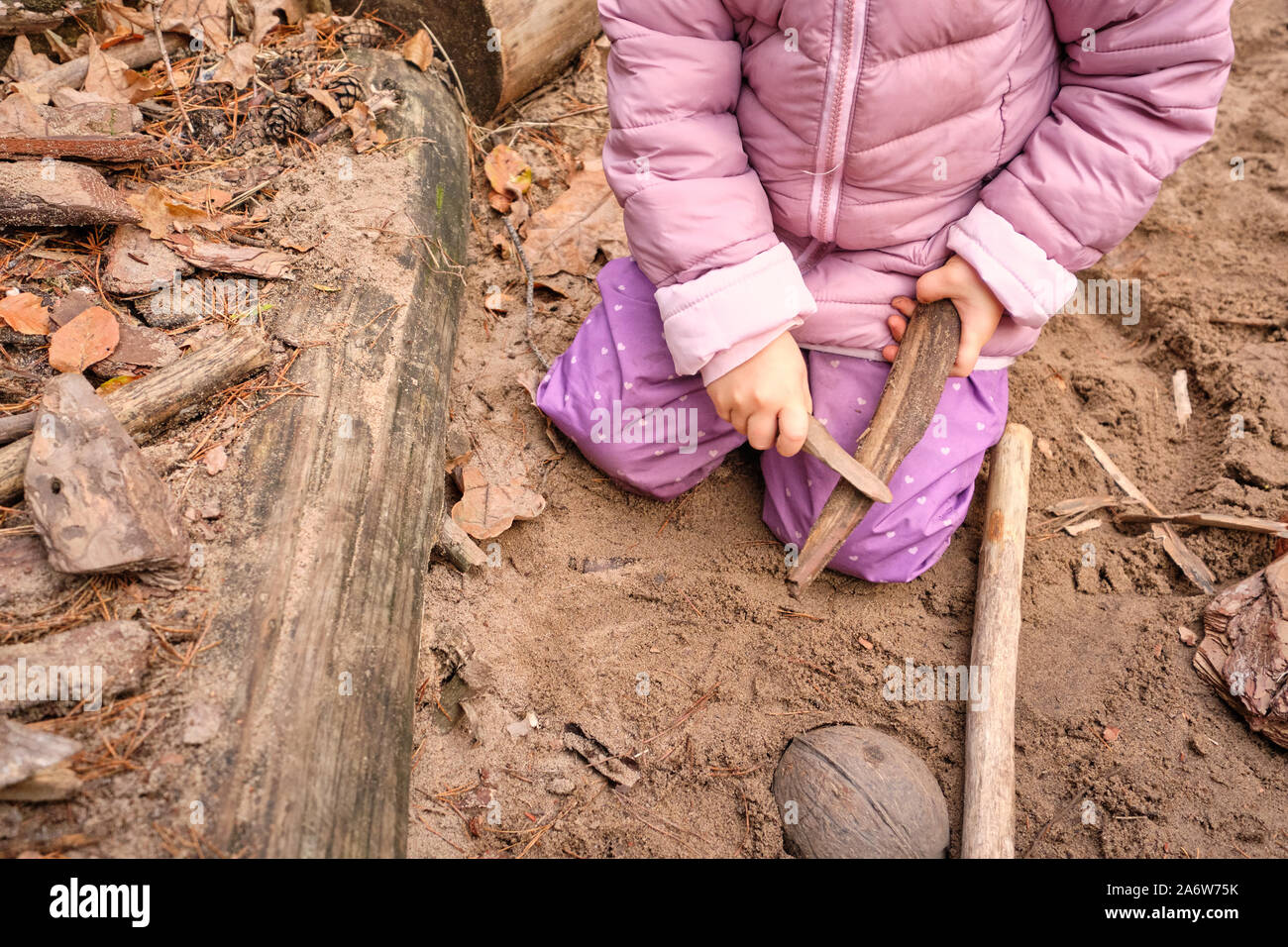 Low section of a child girl playing with wood on a playground in the forest wearing warm clothes in autumn. Seen in Germany, Bavaria in October. Stock Photo