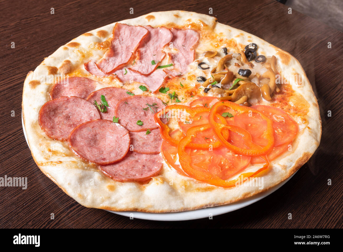 Cheap pizza 4 seasons. With ham, pepperoni, mushrooms, and tomatoes. Stock Photo