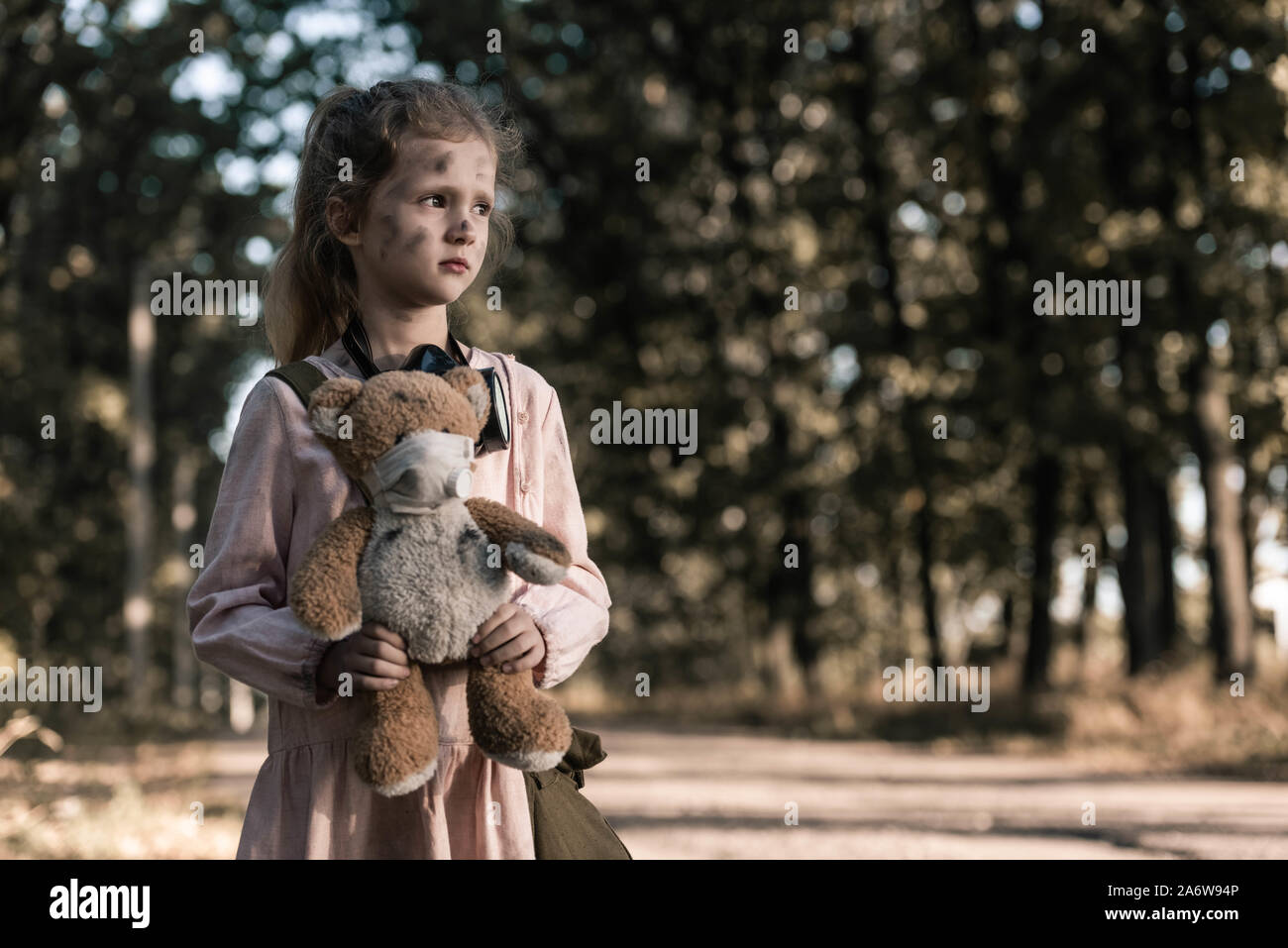 cute kid holding dirty teddy bear near trees in chernobyl, post apocalyptic concept Stock Photo