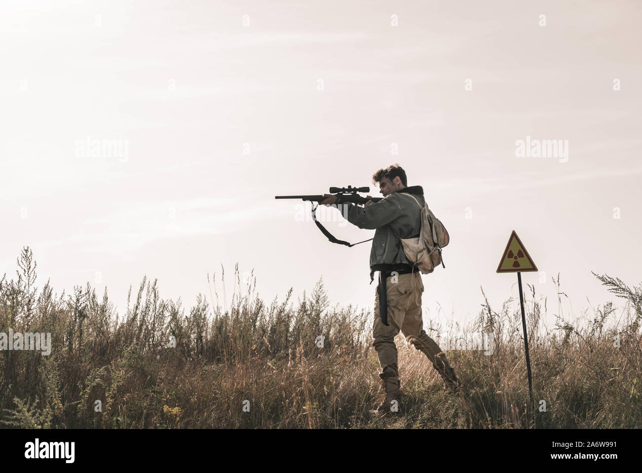 handsome man holding gun near toxic symbol in field, post apocalyptic concept Stock Photo
