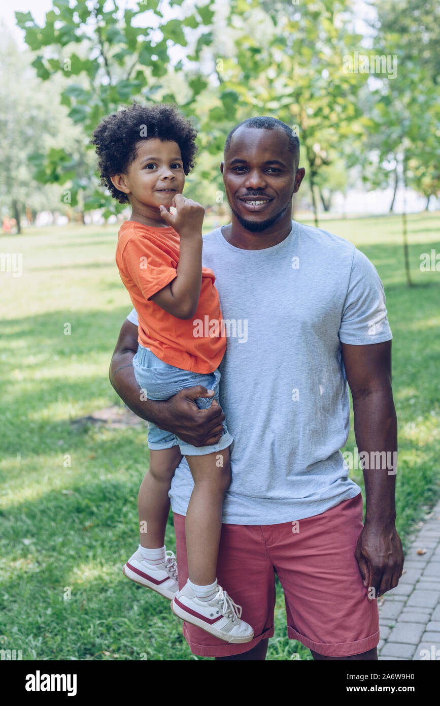 happy african american man holding adorable son and looking at camera ...