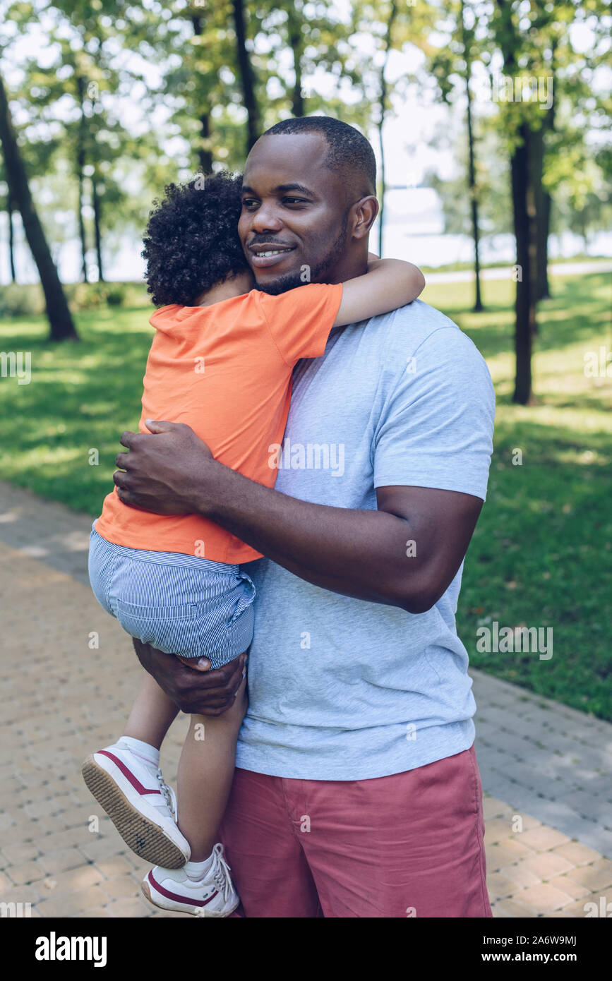 happy african american man holding on hands and embracing adorable son ...