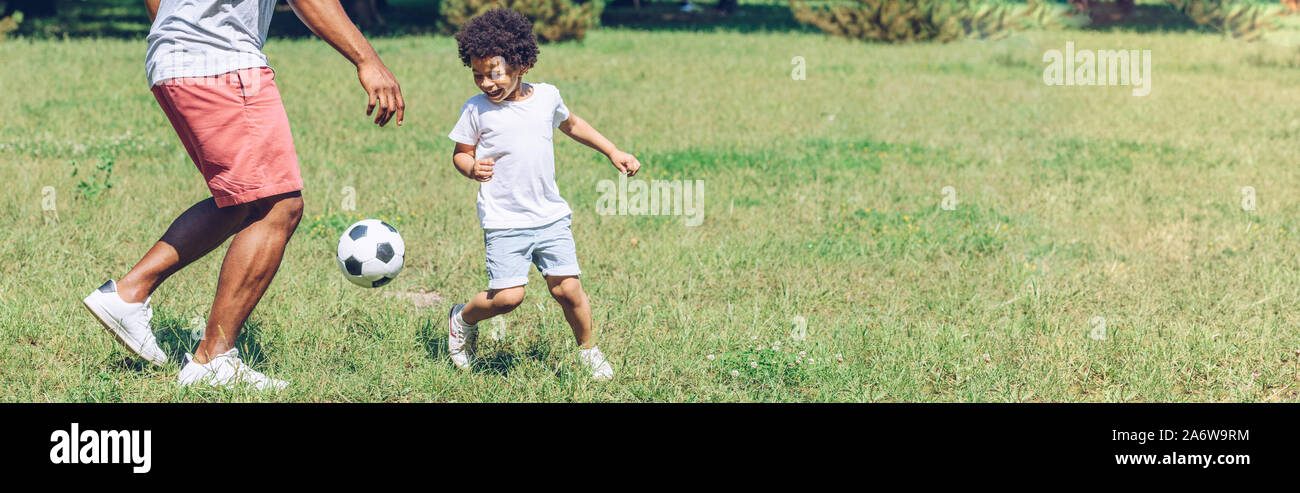 panoramic shot of african american father and son playing football in ...