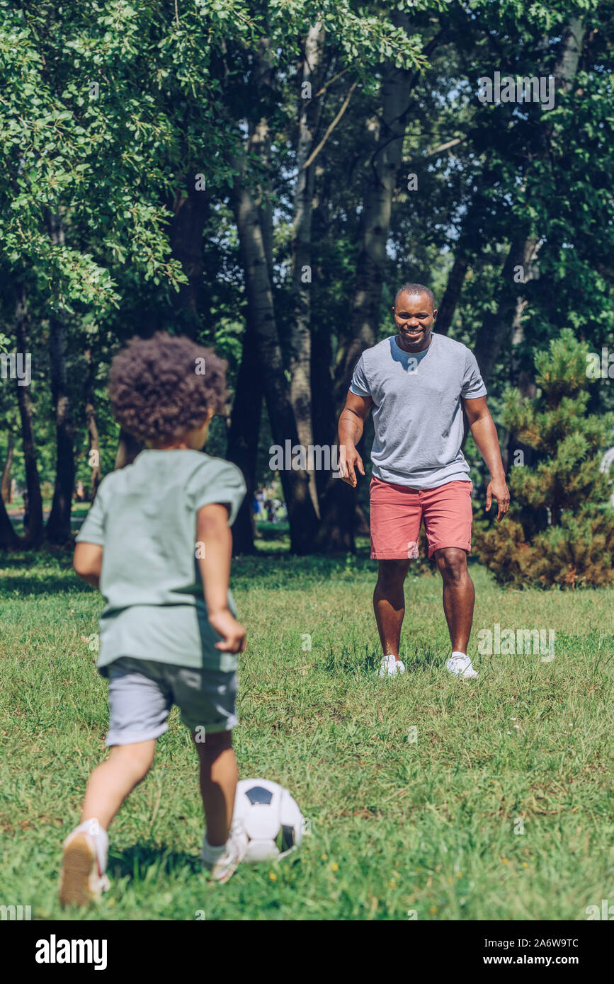 young african american father playing football with adorable son in ...