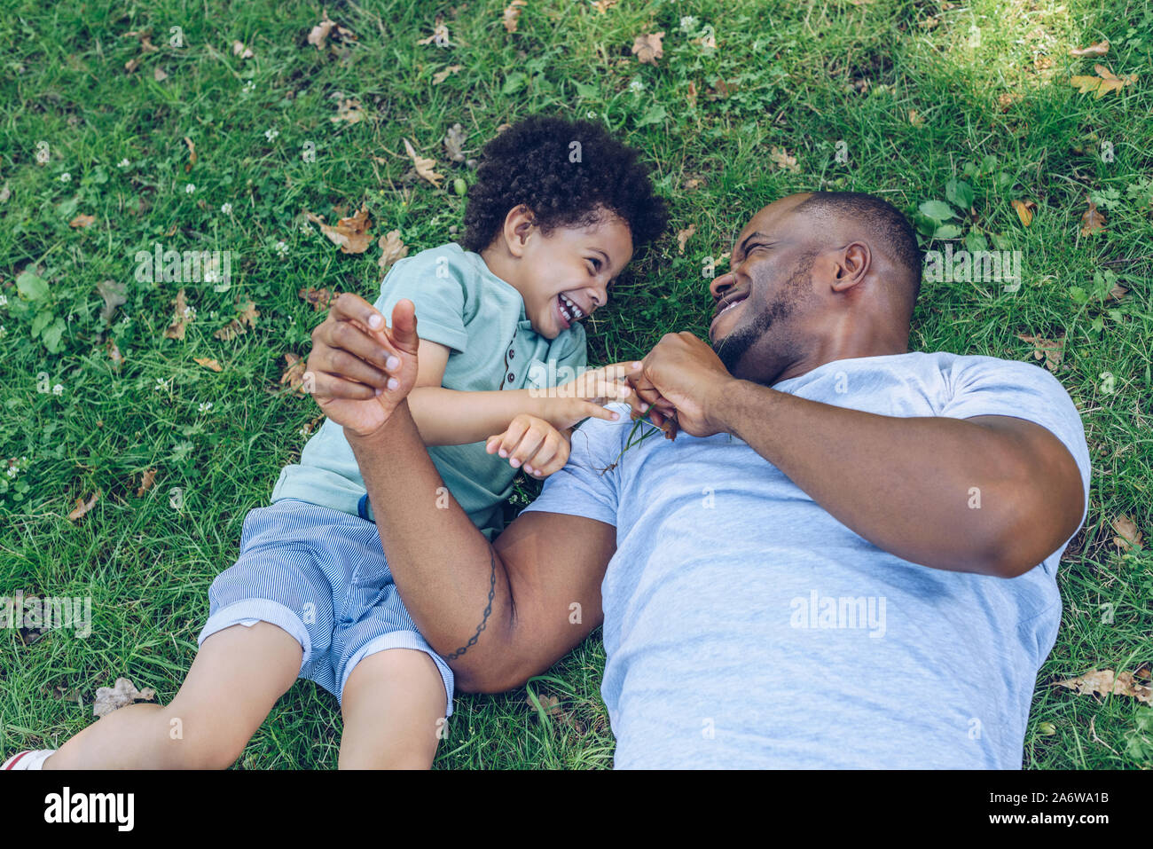 happy african american father and son having fun while lying on lawn in ...