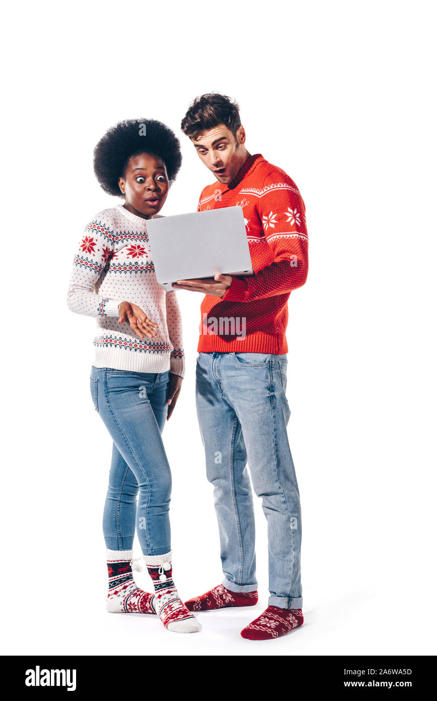 surprised multicultural couple in sweaters using laptop, isolated on white Stock Photo