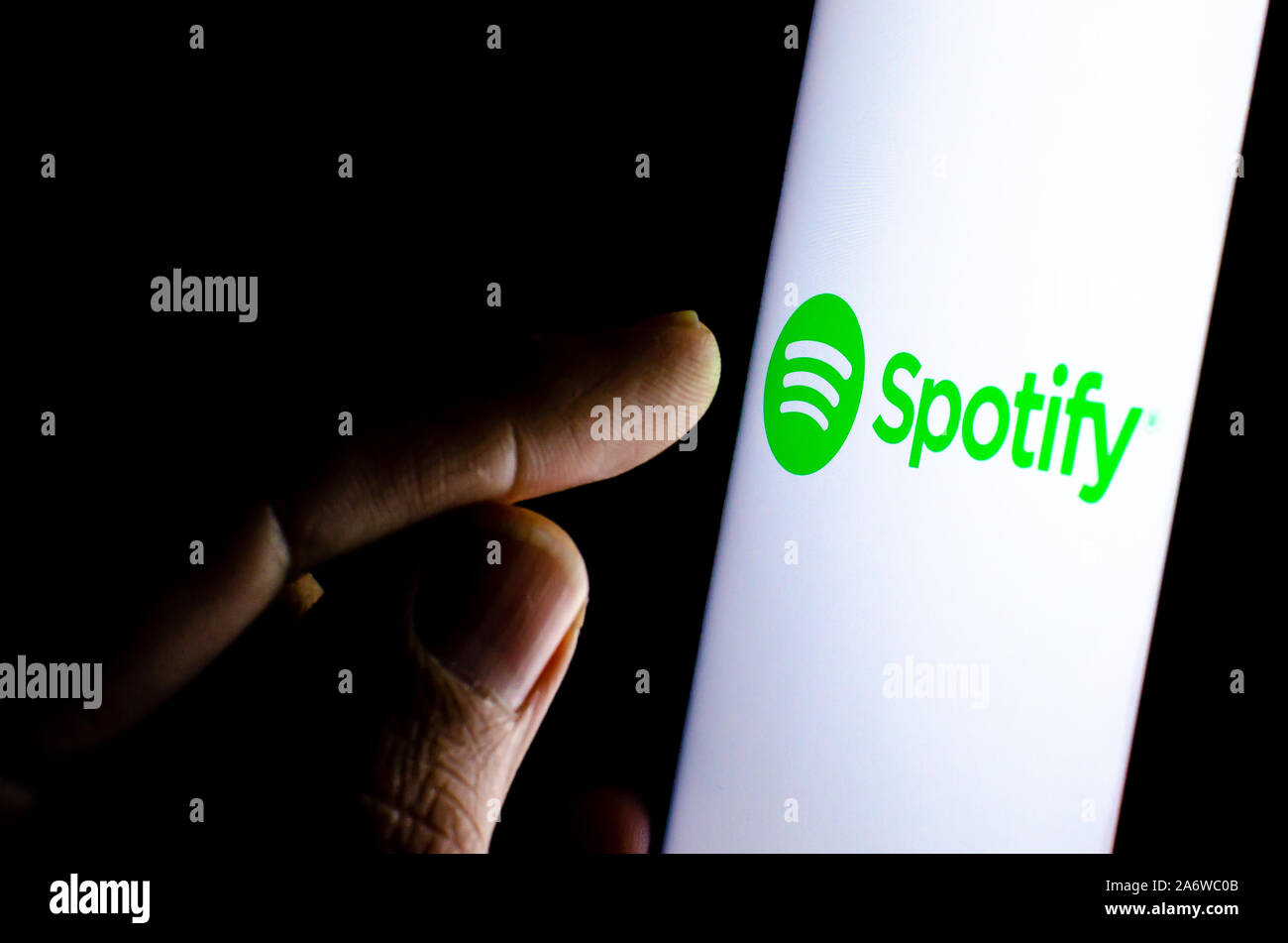 Spotify logo on a smartphone screen in a dark room and a finger touching it. Stock Photo
